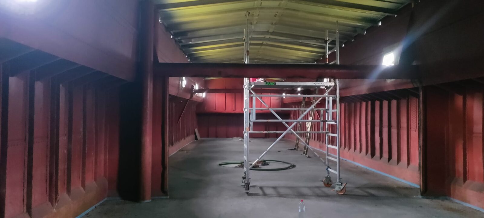 Industriële hal met rode staalstructuur tijdens de schilderwerken, met rolsteiger in het midden